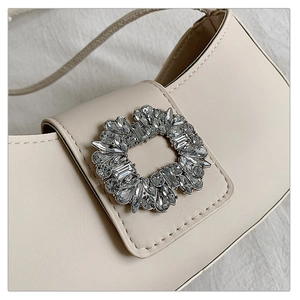 Détail d'un sac demi-lune crème avec une boucle ornée de cristaux étincelants