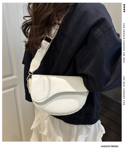 Detailed side view of a white leather saddle bag with wide strap and gold hardware