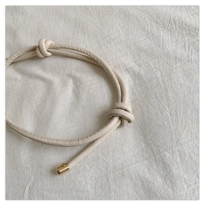 Détail de la bandoulière en cuir beige minimaliste avec nœuds et embouts métalliques dorés