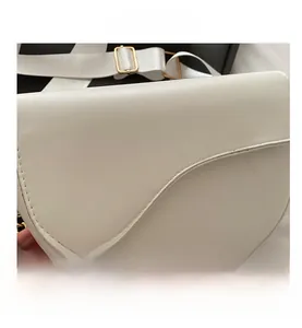 Macro view of white saddle bag with wide fabric strap and golden metallic hardware