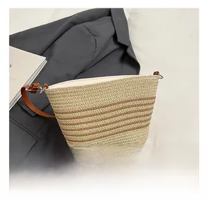 Détail d'un sac bandoulière en paille rayé beige et marron sur un blazer gris