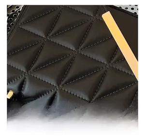 Detail of black quilted shoulder bag with triangular stitching and golden metal hardware