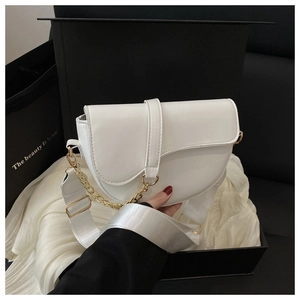 Close-up of white saddle bag with golden chain and wide fabric strap on black gift box