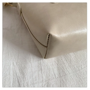 Detail shot of cream tote bag featuring golden metal ring and premium stitched edges