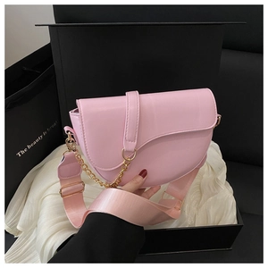 Pink leather saddle bag with gold chain and woven strap displayed in a gift box