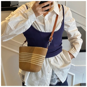 Détail d'un sac seau en paille tressée avec bandoulière en cuir et texture rayée naturelle