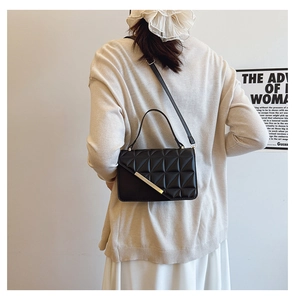 Detail of black quilted shoulder bag with gold metal trim on elegant lady outfit