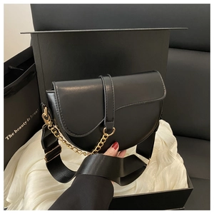 Detail of black saddle bag with golden chain and woven strap on silk background