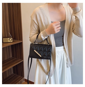Detail of black quilted shoulder bag with gold metal trim in a cozy indoor setting