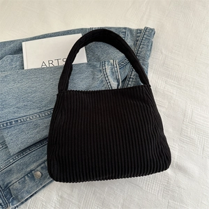 Minimalist black corduroy shoulder bag displayed on fabric with artistic accessories