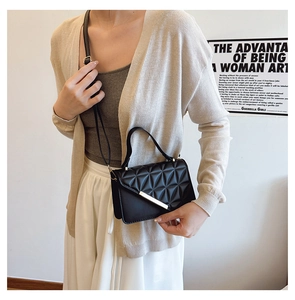 Detail of black quilted shoulder bag featuring geometric patterns and gold metal clasp