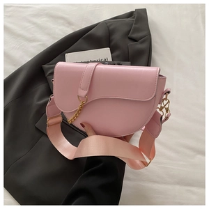 Detail of pink saddle bag featuring a gold chain accent and wide fabric shoulder strap