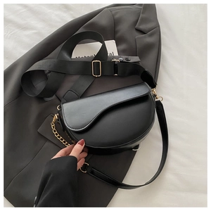 Detail of black matte saddle bag with wide fabric strap and golden metal chain