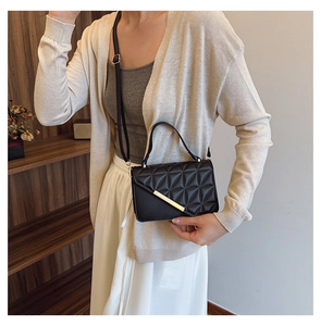 Detail of a black quilted leather crossbody bag with elegant gold metal hardware bar
