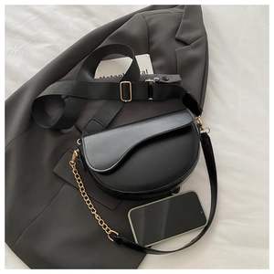 Detail of black matte saddle bag with nylon strap and gold chain against dark blazer