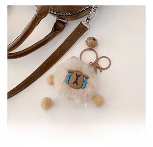 Détail d'un porte-clés en peluche marron clair avec visage bleu sur un sac en cuir