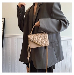 Detail of beige quilted crossbody bag with geometric stitching held by a model