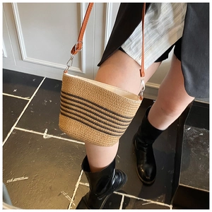 Dettaglio borsa a secchiello in paglia beige con strisce nere e tracolla in pelle