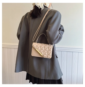 Detail of beige quilted crossbody bag with golden buckle on grey oversized blazer