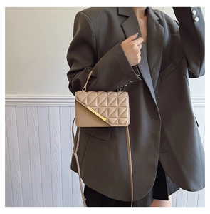 Close-up of quilted beige crossbody bag with gold detail on a grey blazer outfit