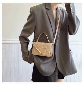 Close-up of beige quilted crossbody bag with gold metal trim worn by a fashion model