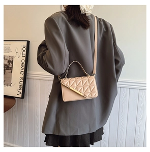 Detail of beige quilted shoulder bag with gold metal trim on elegant model outfit