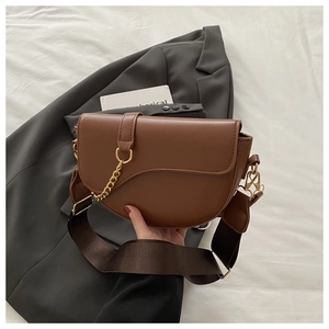 Detail of a brown saddle bag with gold chain and a wide adjustable canvas strap