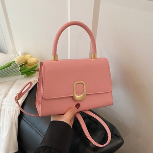 Pink minimalist crossbody bag with golden oval lock on a black leather stool