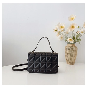 Detail of black quilted leather handbag with gold hardware and top handle on white desk