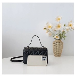 Detailed view of black quilted mini handbag next to a smartphone for size reference