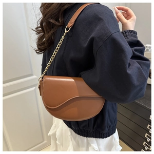 Detail view of brown leather saddle bag with gold chain strap worn as a crossbody purse