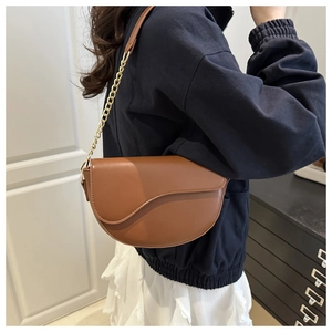 Caramel brown saddle bag featuring elegant metal chain strap shown on model's shoulder