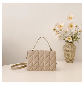 Close-up of beige quilted crossbody bag with geometric stitching on white tabletop