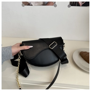 Detail of black saddle bag featuring vintage asymmetric flap and golden chain accessory