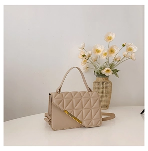 Close-up of quilted beige crossbody bag featuring gold metal bar and elegant handle