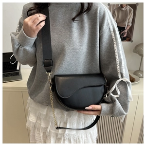 Detail of black matte saddle bag featuring wide fabric strap and gold metal chain