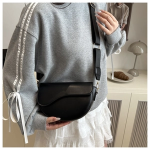 Classic black leather saddle bag with wide strap styled in a minimalist home setting