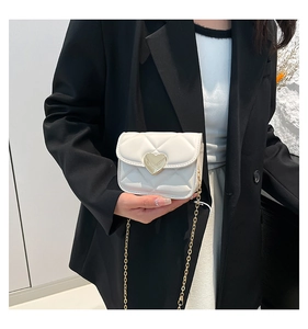 Macro shot of a white quilted mini bag featuring a gold heart-shaped metal twist lock
