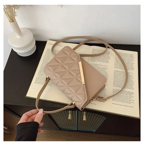 Close-up of beige quilted crossbody bag with gold metal bar and adjustable strap on a book