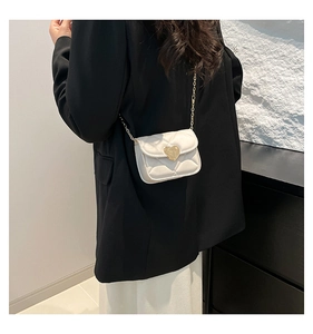 Detailed view of cream quilted mini crossbody bag with heart clasp worn by a model