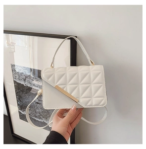 Detail of white quilted crossbody bag with gold metal bar and stylish top handle