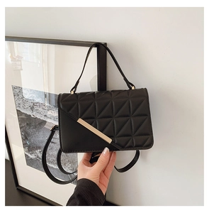 Detail of black quilted shoulder bag with gold metal trim and triangular stitching