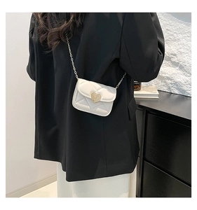 Detail of white quilted mini chain bag with a gold heart clasp on a female model