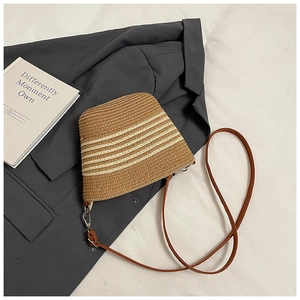 Dettaglio borsa tote in paglia intrecciata con strisce crema e tracolla marrone sottile