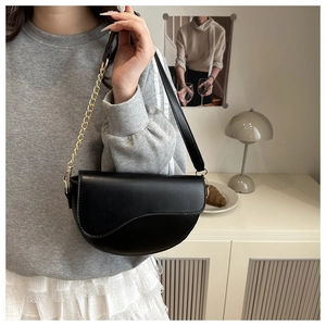 Detail of black saddle bag with gold chain strap shown in a modern home interior