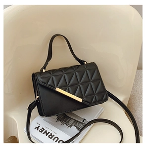 Detail of black quilted crossbody bag with gold hardware on a minimalist chair