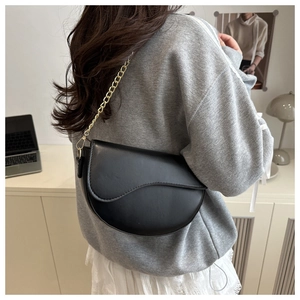Side view of a black leather saddle bag with gold chain strap on a female model