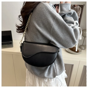 Detail of a chic black saddle bag with gold chain strap on a model in a modern room
