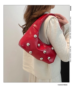 Détail d'un sac demi-lune rouge en cuir brillant avec rivets argentés porté par un mannequin