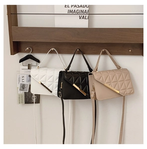 Detail of quilted leather crossbody bags in white, black and beige with gold V-shape buckle